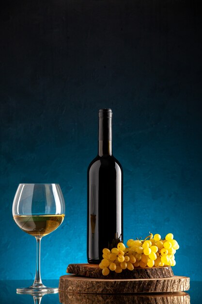 Vista frontal de la botella de vino negro copa de vino uvas frescas sobre tablero de madera en el cuadro azul