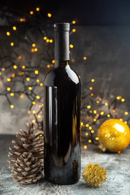 Vista frontal de la botella de vino tinto para la celebración y dos conos de coníferas sobre fondo oscuro
