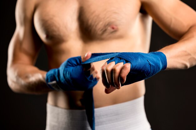 Vista frontal del boxeador masculino poniéndose protección para las manos