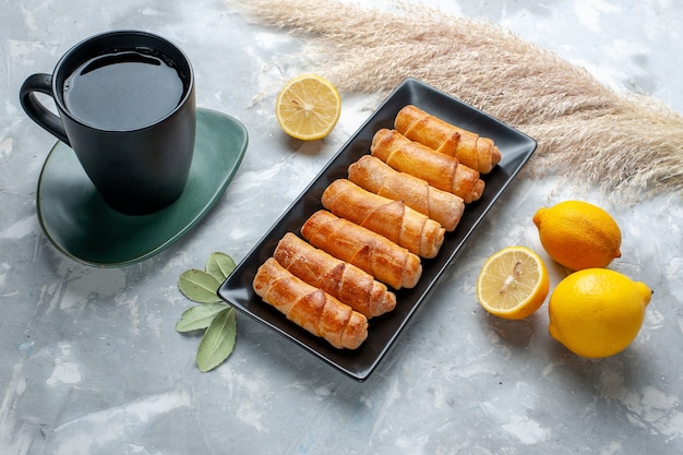 Vista frontal brazaletes dulces con limón y una taza de té en la mesa de luz, pastel de pastelería hornear azúcar dulce