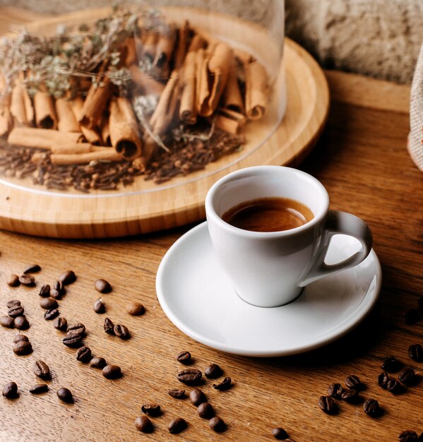 Vista frontal de café junto con canela y semillas de café alrededor en el piso de madera marrón
