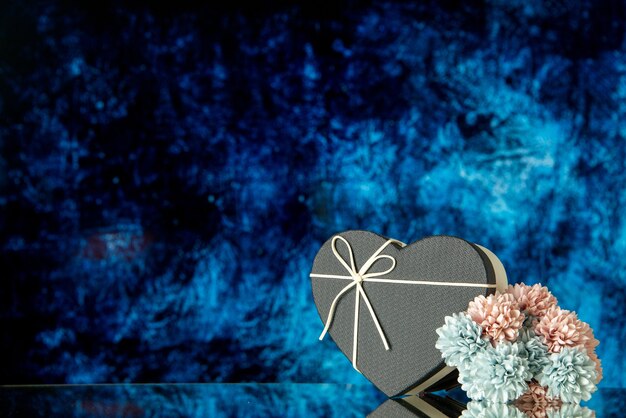 Vista frontal de la caja de corazón negro flores de colores sobre fondo abstracto azul oscuro