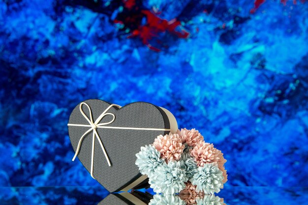 Vista frontal de la caja de regalo de corazón con tapa negra y flores de colores sobre fondo abstracto azul