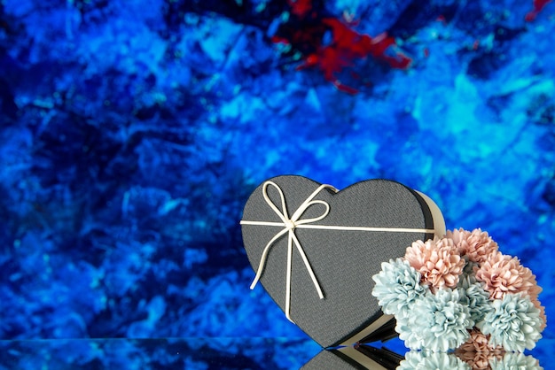 Vista frontal de la caja de regalo de corazón con tapa negra y flores de colores sobre fondo abstracto azul