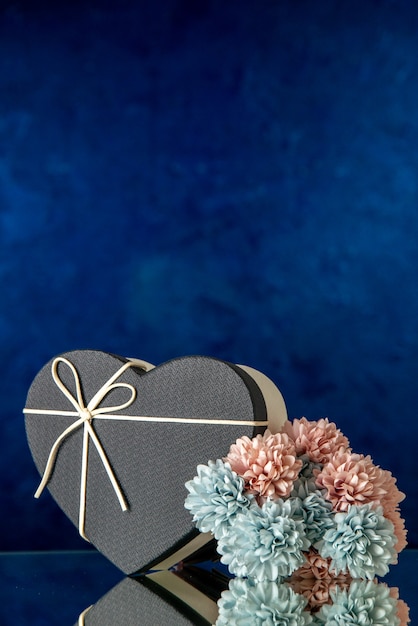 Vista frontal de la caja de regalo con forma de corazón con flores de colores de tapa negra sobre fondo oscuro