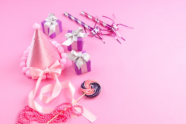 Una vista frontal cajas de regalo de color púrpura junto con silbatos de cumpleaños gorro de piruleta rosa sobre rosa