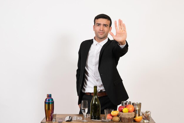 Vista frontal del camarero masculino en traje clásico de pie frente a la mesa con bebidas en el escritorio blanco alcohol bar club bebida masculina noche