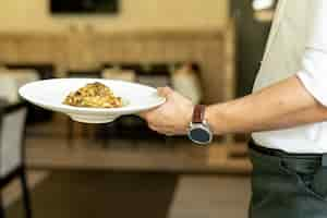 Foto gratuita vista frontal del camarero sosteniendo un plato con pasta