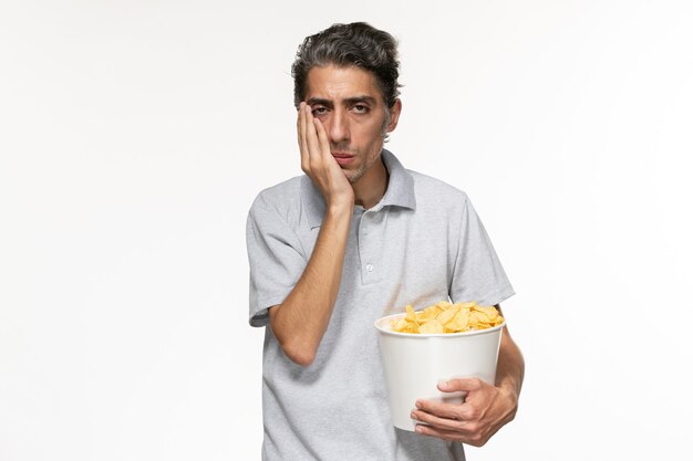 Vista frontal de la canasta de explotación masculina joven con papas fritas deprimido sobre la superficie blanca