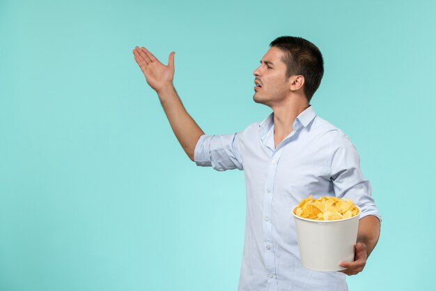 Vista frontal de la canasta de explotación masculina joven con papas fritas en el escritorio azul