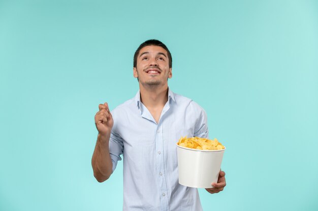 Vista frontal de la canasta de explotación masculina joven con papas fritas en el escritorio azul