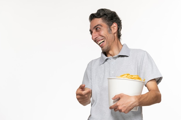 Vista frontal de la canasta de explotación masculina joven con papas fritas hablando con alguien sobre la superficie blanca