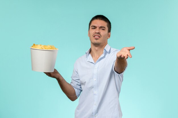 Vista frontal de la canasta de explotación masculina joven con papas fritas en la superficie azul claro