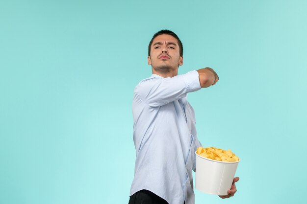 Vista frontal de la canasta de explotación masculina joven con papas fritas en la superficie azul claro