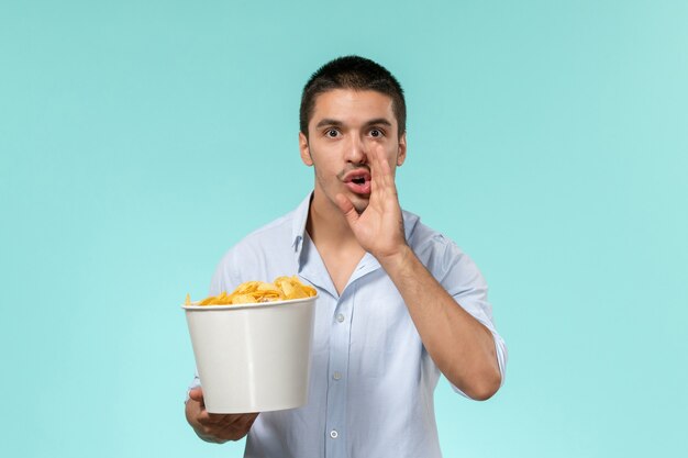 Vista frontal de la canasta de explotación masculina joven con papas fritas en la superficie azul claro