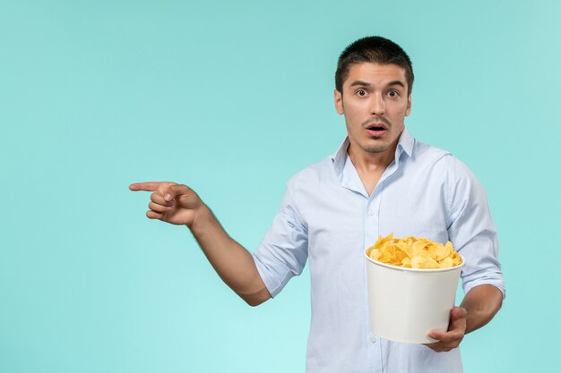 Vista frontal de la canasta de explotación masculina joven con papas fritas en la superficie azul