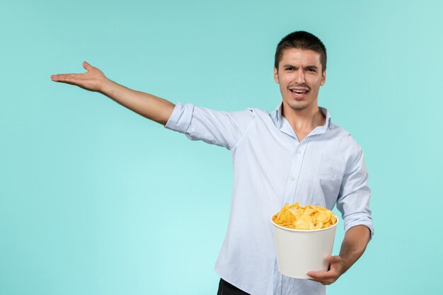 Vista frontal de la canasta de explotación masculina joven con papas fritas en la superficie azul