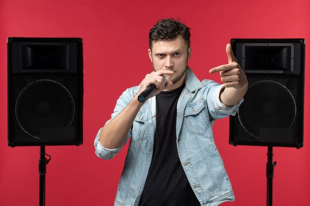 Vista frontal del cantante masculino actuando en el escenario con micrófono en pared roja