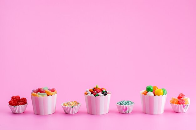 Una vista frontal de caramelos de colores dentro de paquetes de papel en rosa, azúcar dulce de color