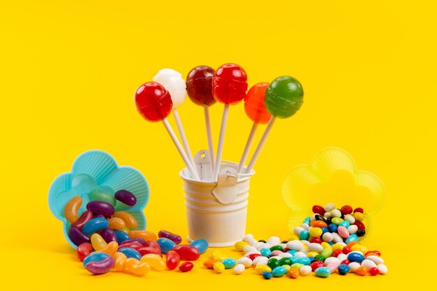 Una vista frontal de caramelos de colores junto con piruletas aisladas en amarillo, dulce color azúcar