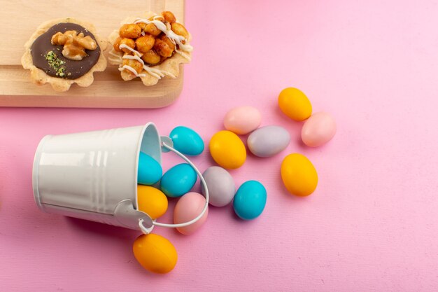Una vista frontal de caramelos de colores con pequeños pasteles de chocolate en el color rosa azúcar de escritorio dulce