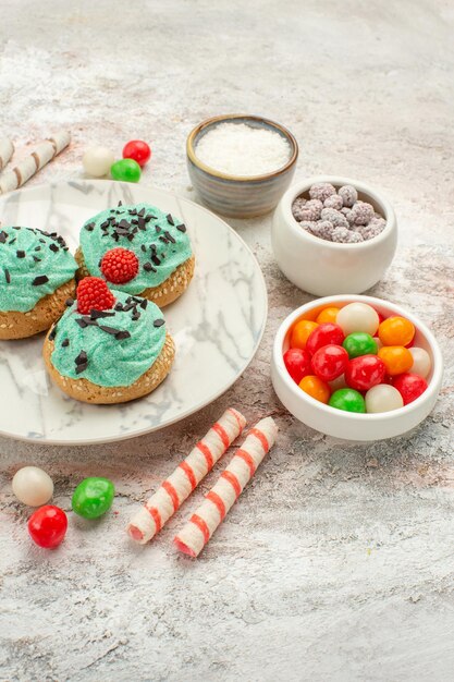 Vista frontal de caramelos de colores con tortas de crema en la galleta de la torta dulce de la galleta del escritorio blanco