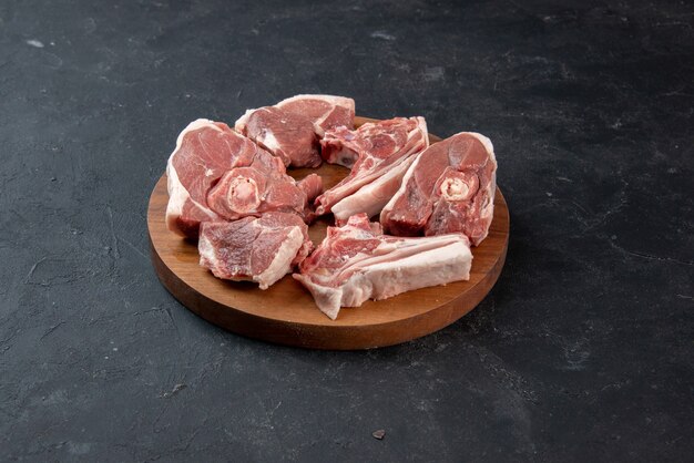 Vista frontal de la carne fresca rebanadas de carne cruda en el escritorio de madera redonda sobre fondo oscuro alimentos frescura animal vaca comida comida cocina