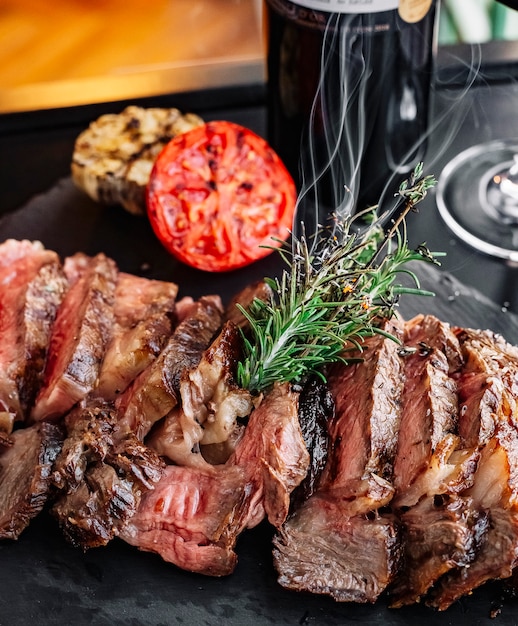 Vista frontal de carne a la parrilla con romero y una rodaja de tomate en el tablero