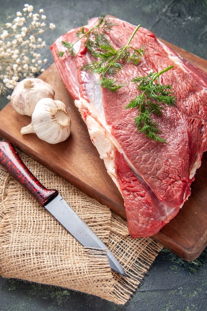 Foto gratuita vista frontal de carnes rojas crudas frescas ajos verdes sal de limón en un cuchillo de tabla de cortar de madera marrón sobre una toalla de color nude sobre fondo de color oscuro