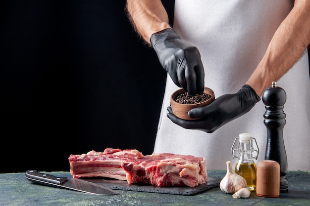 Vista frontal de carnicero macho vertiendo pimienta en una rebanada de carne sobre una superficie oscura