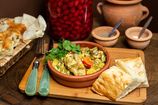 Una vista frontal de cerca comida cocinada dentro de una olla redonda marrón junto con rebanadas de pan