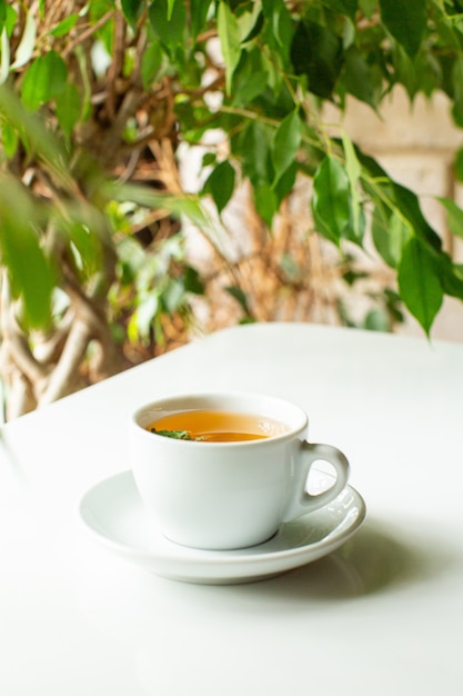 Una vista frontal de cerca té caliente dentro de una taza blanca en el piso blanco