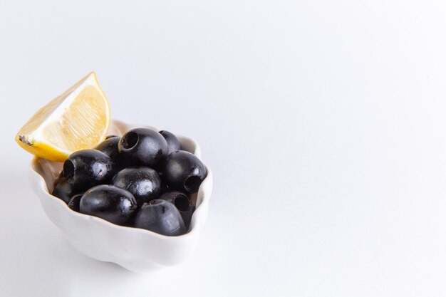 Vista frontal cercana aceitunas negras frescas con una rodaja de limón en la superficie blanca foto en color aceite vegetal de alimentos