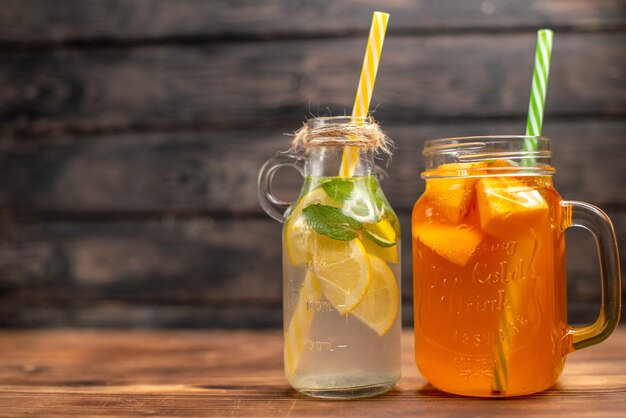 Vista frontal cercana de agua de desintoxicación fresca y jugo de frutas servido con tubos en el lado izquierdo sobre un fondo marrón