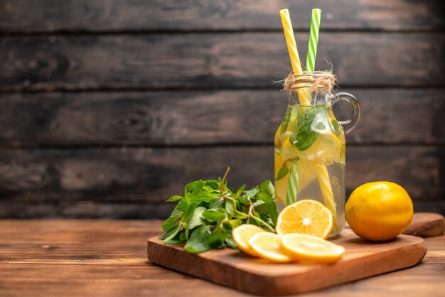 Vista frontal cercana de agua de desintoxicación fresca natural servida con un tubo de menta y naranja en el lado izquierdo sobre un fondo marrón