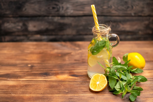 Vista frontal cercana de agua de desintoxicación fresca natural servida con un tubo de menta y naranja en el lado izquierdo sobre un fondo marrón