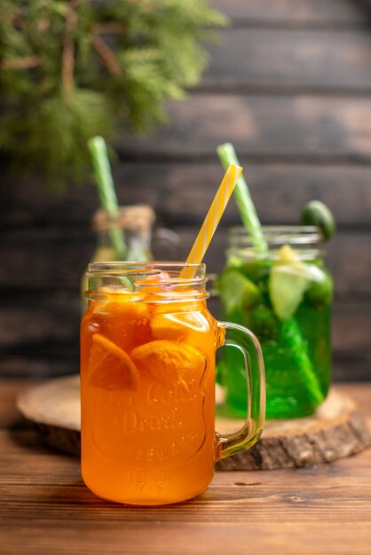 Vista frontal cercana de agua de desintoxicación y jugo fresco en botellas con tubos sobre fondo de madera marrón