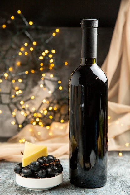 Vista frontal cercana de la botella de vino tinto para la celebración familiar servida con frutas en una olla blanca sobre fondo oscuro