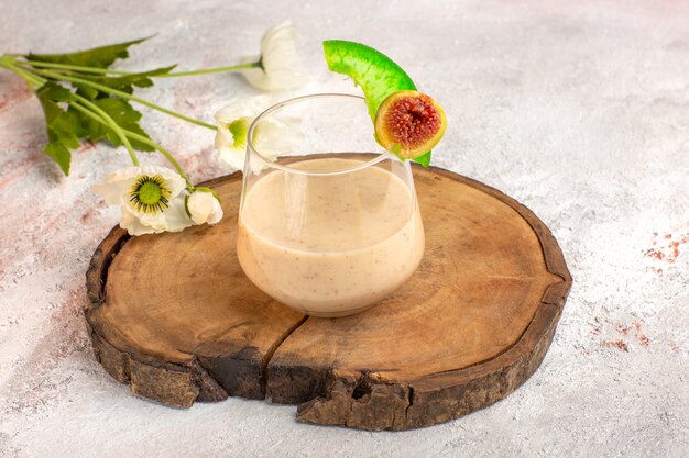 Vista frontal cercana cóctel cremoso dentro de un pequeño vaso con flores en la superficie blanca