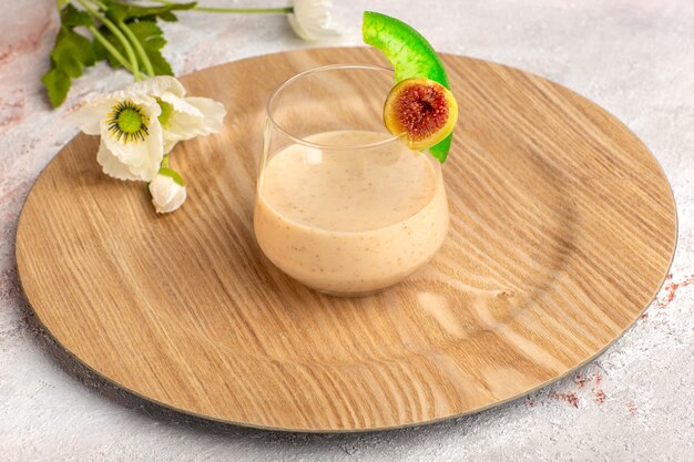 Vista frontal cercana cóctel cremoso dentro de un pequeño vaso con flores en la superficie blanca