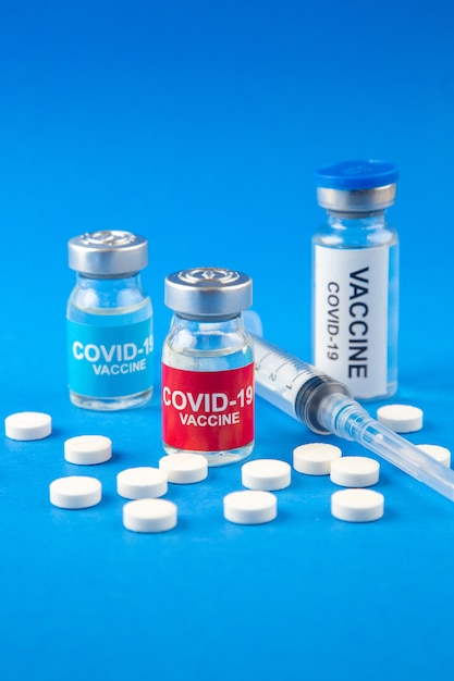 Vista frontal cercana de COVID- vacunas en ampollas médicas píldoras jeringa desechable sobre fondo azul oscuro y suave