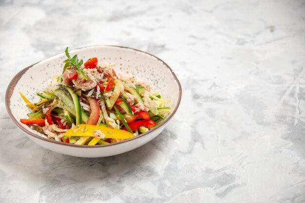 Vista frontal cercana de una deliciosa ensalada de pollo con verduras en el lado derecho sobre una superficie blanca manchada con espacio libre