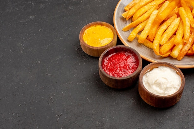 Vista frontal cercana deliciosas papas fritas con condimentos en el espacio oscuro