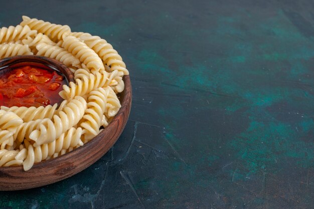 Vista frontal cercana en forma de pasta italiana con salsa de tomate sobre superficie azul oscuro