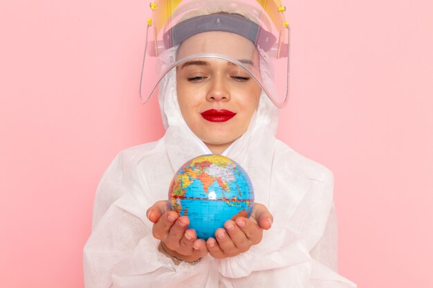 Vista frontal cercana joven hermosa mujer en traje blanco especial con casco protector sosteniendo pequeño globo en rosa