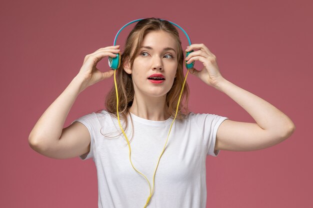 Vista frontal cercana joven mujer atractiva escuchando música a través de auriculares en la pared rosa modelo color hembra joven