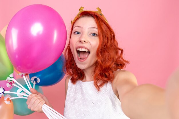 Vista frontal cercana joven sosteniendo globos de colores regocijándose en rosa