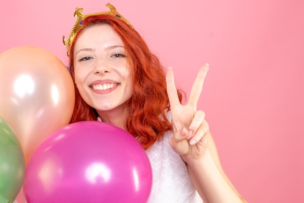 Vista frontal cercana joven sosteniendo globos de colores y sonriendo a la cámara en rosa