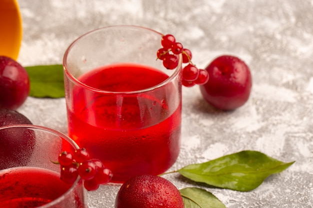 Vista frontal cercana jugo de ciruela roja con ciruelas frescas en la superficie de la luz