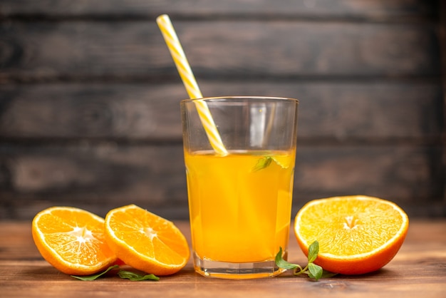 Vista frontal cercana de jugo de naranja fresco en un vaso servido con un tubo de menta y limas de naranja sobre una mesa de madera